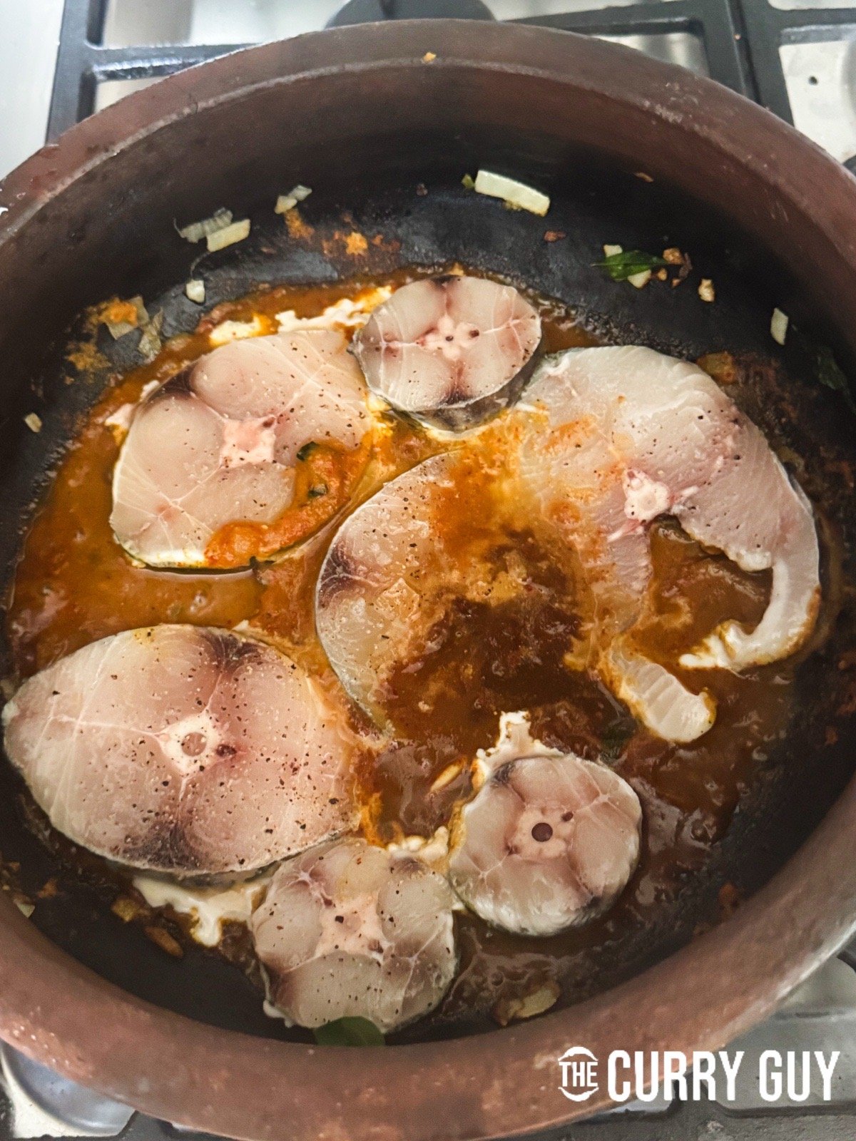 Adding the fish pieces to the simmering sauce in the pan.