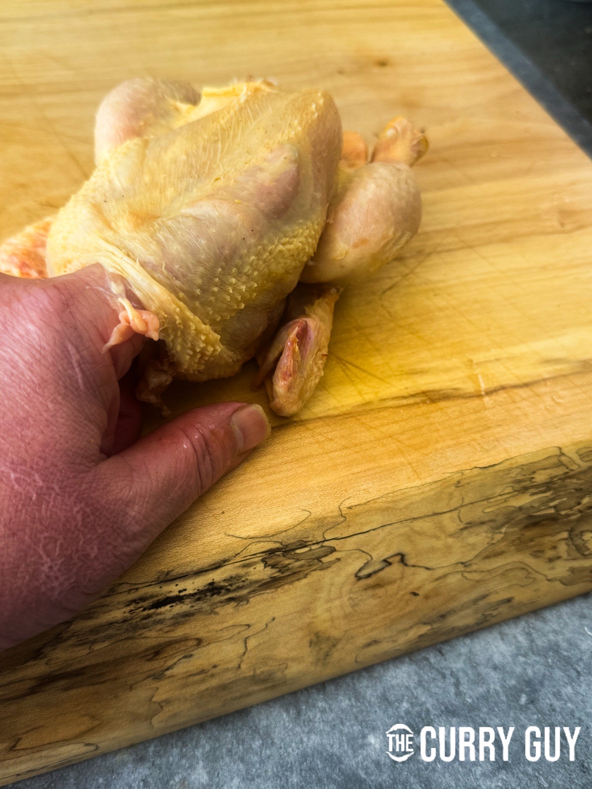 Running a finger underneath the skin of the chicken to separate the skin and meat.