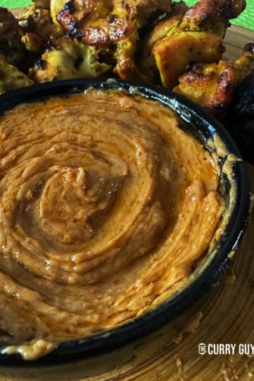Thai peanut sauce in a serving bowl next to Thai grilled chicken.