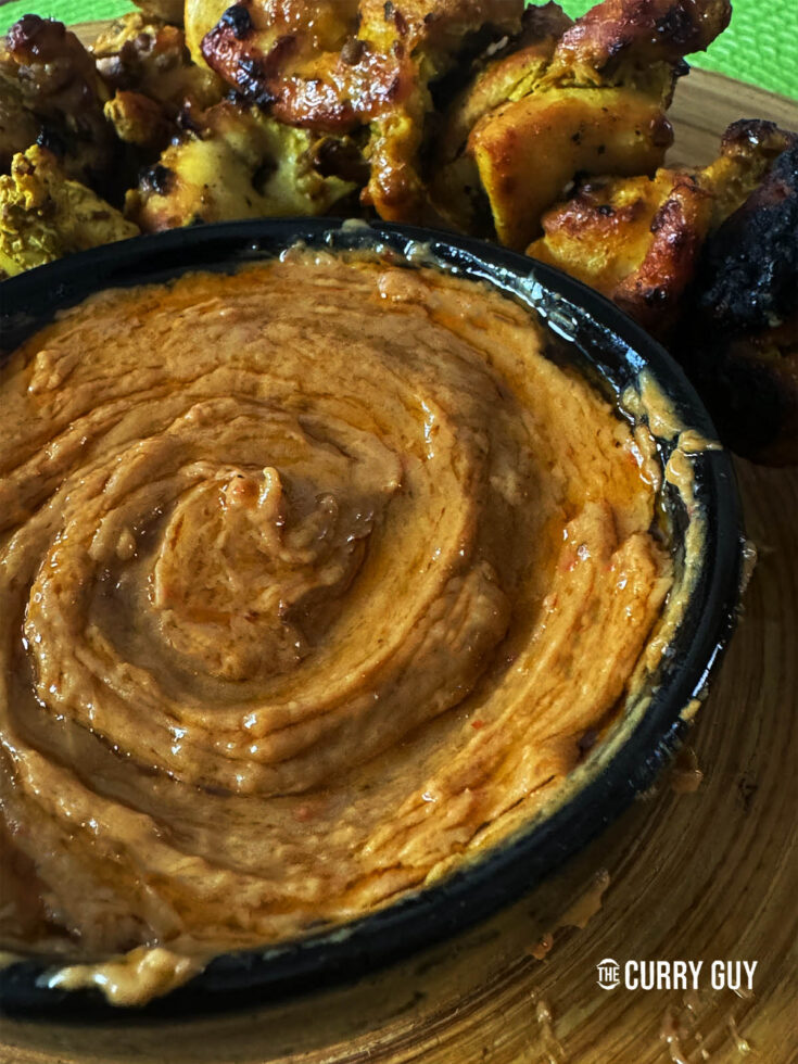 Thai peanut sauce in a serving bowl next to Thai grilled chicken.
