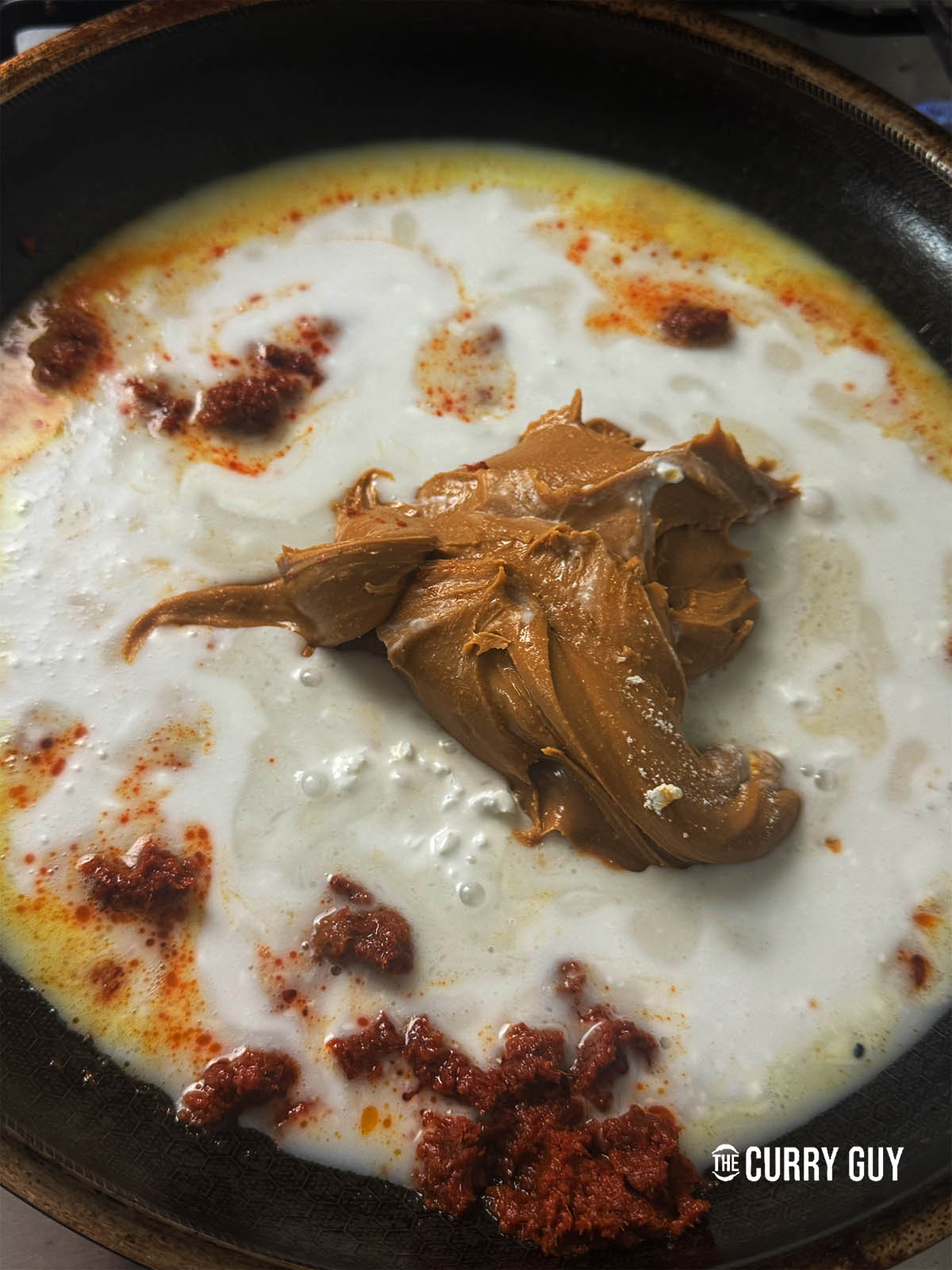 Adding coconut milk and peanut butter to the Thai red curry paste in the pan.