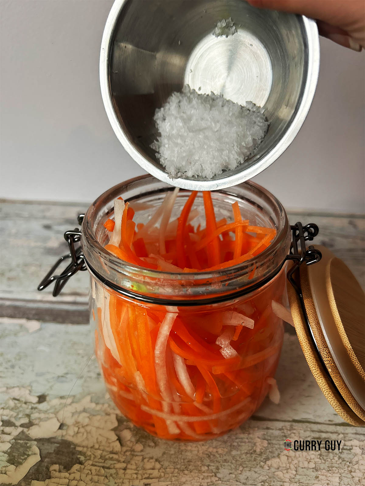 Pouring salt over the carrots and daikon in the jar.