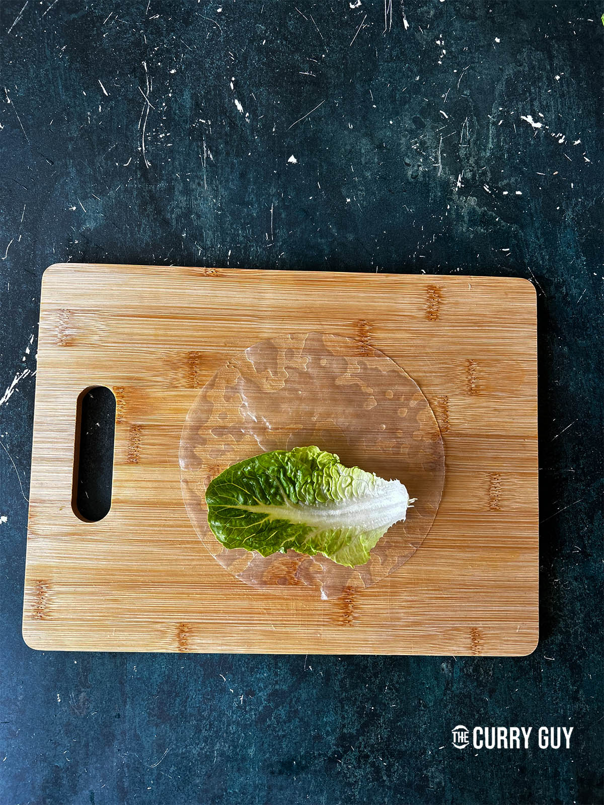 Placing the soaked rice paper on a board and placing a piece of lettuce on top.
