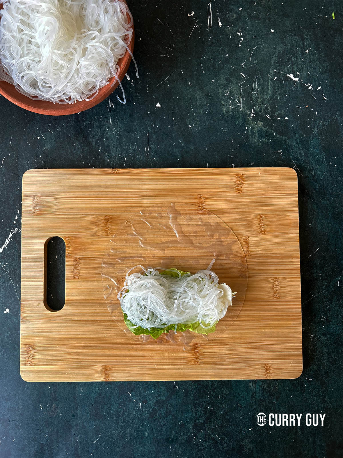 Topping the piece of lettuce with a small mound of cooked rice vermicelli noodles.