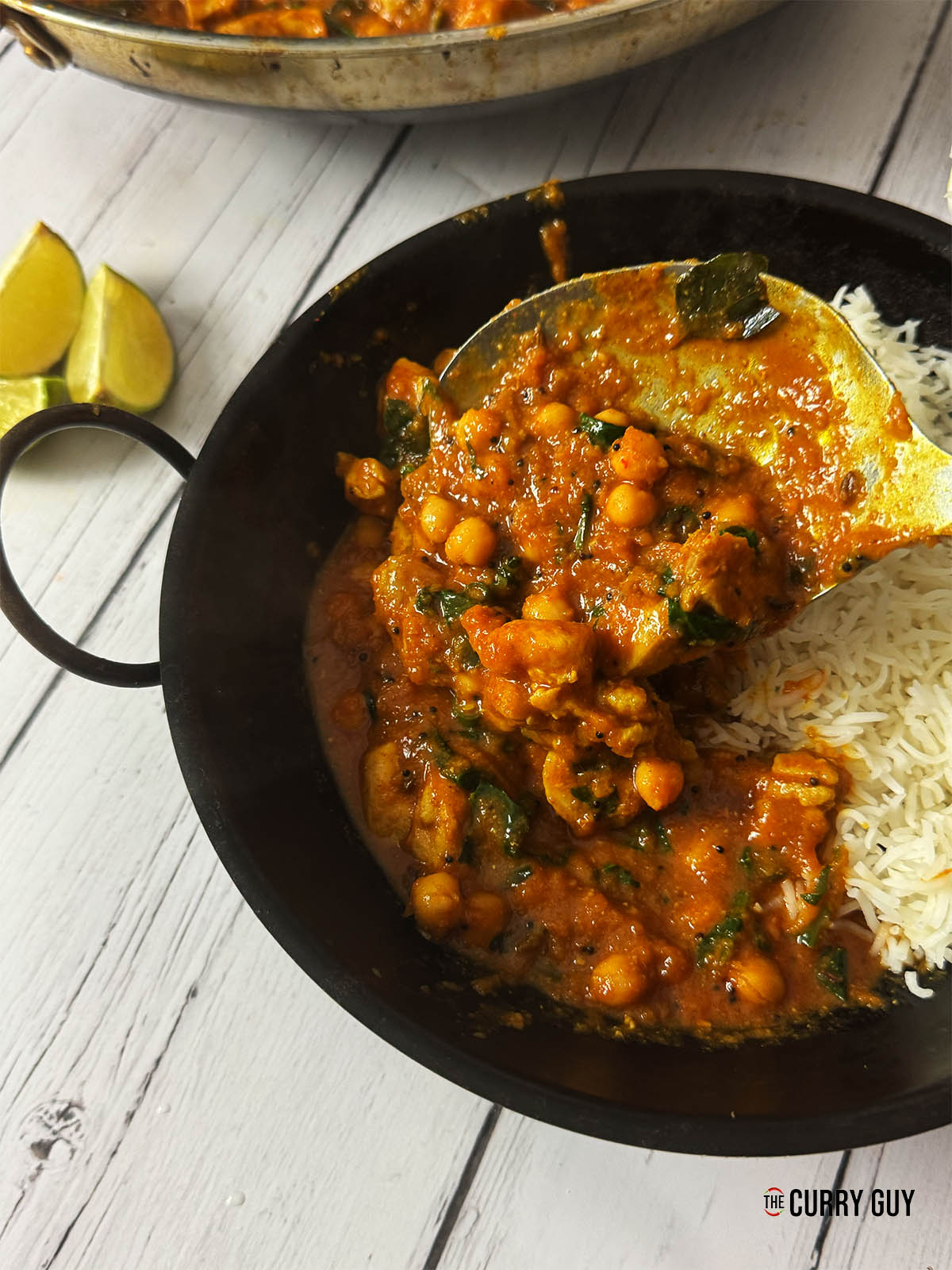Chicken and chickpea curry being spooned into a serving bowl at the table.