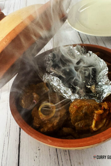 Adding the burning charcoal on a piece of foil to the curry to smoke.