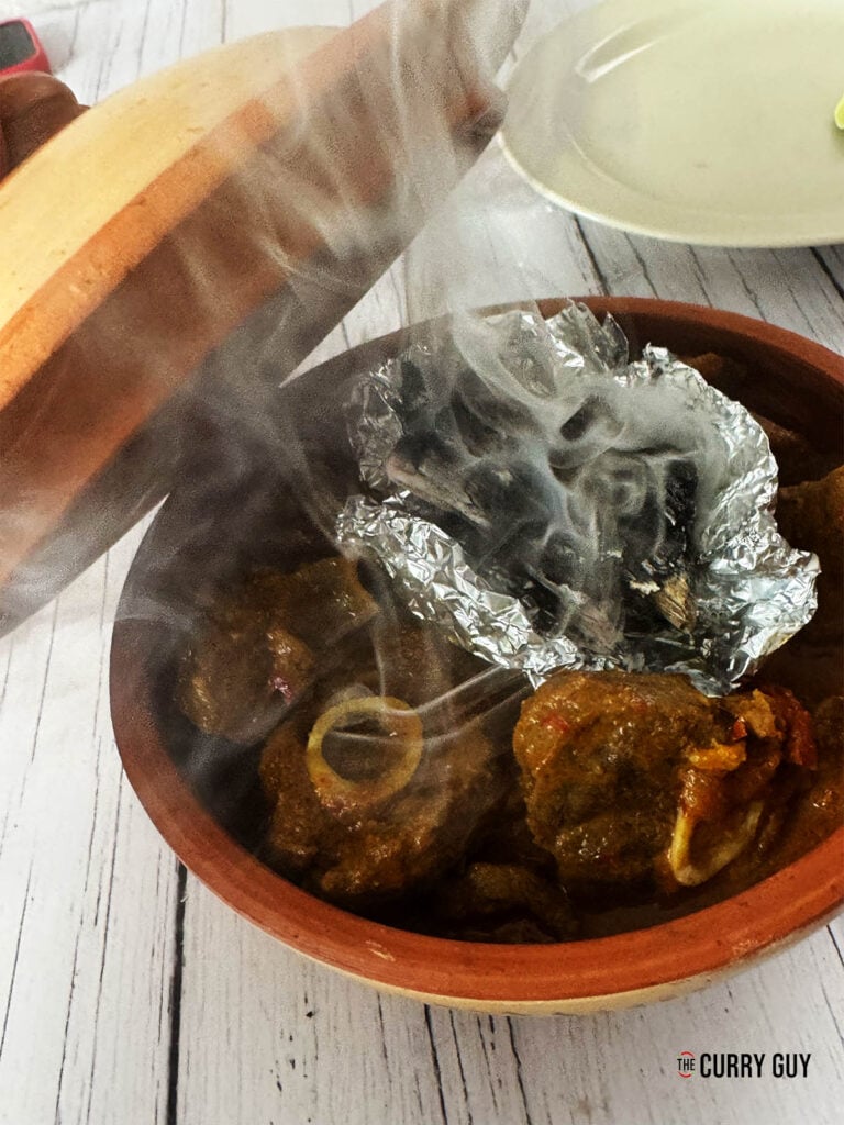 Adding the burning charcoal on a piece of foil to the curry to smoke.