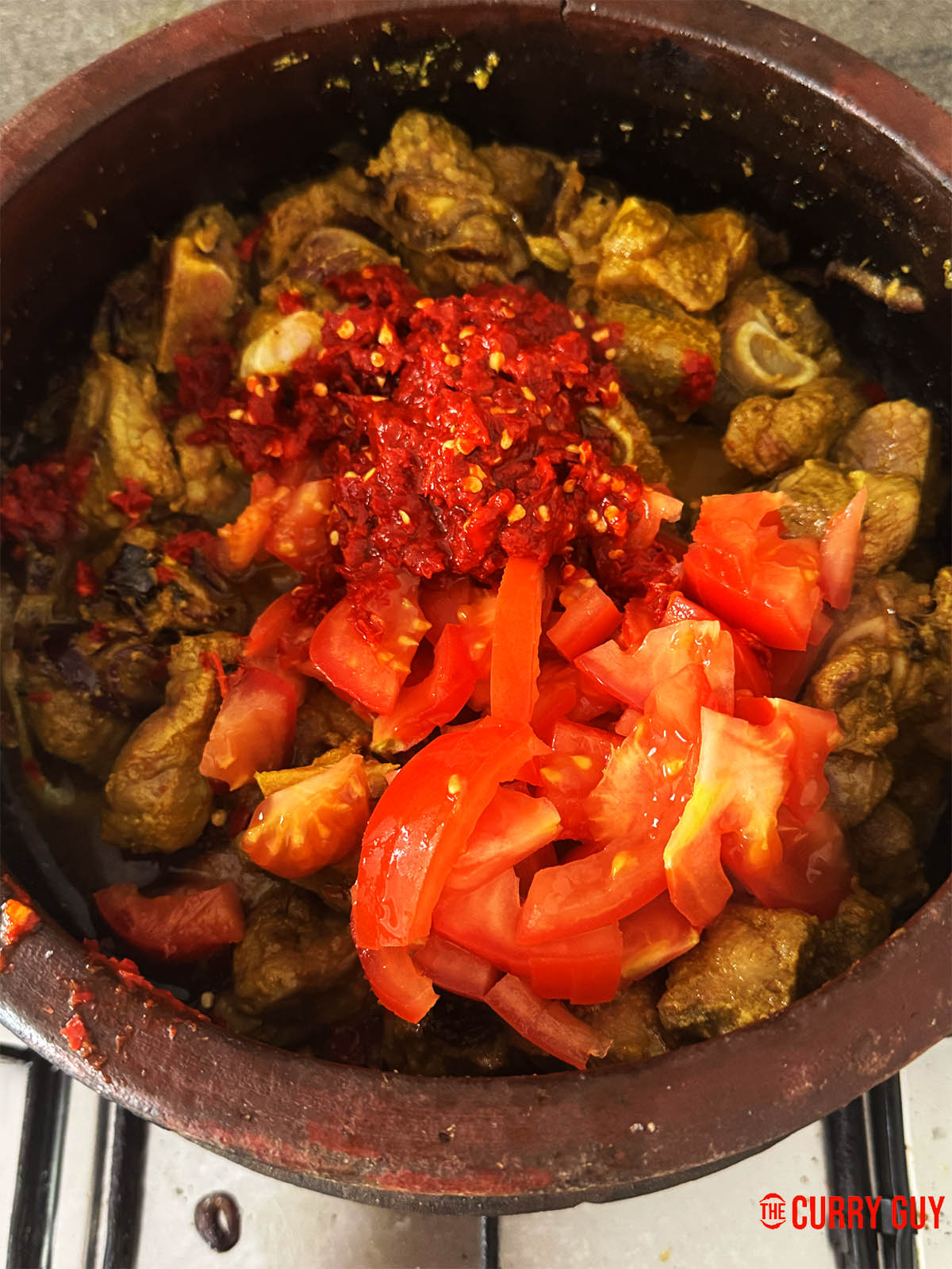 Adding the chilli paste and diced tomatoes to the lamb.