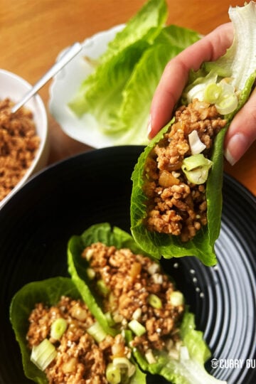 Pork lettuce wraps. Two on a plate and one being held ready to eat.