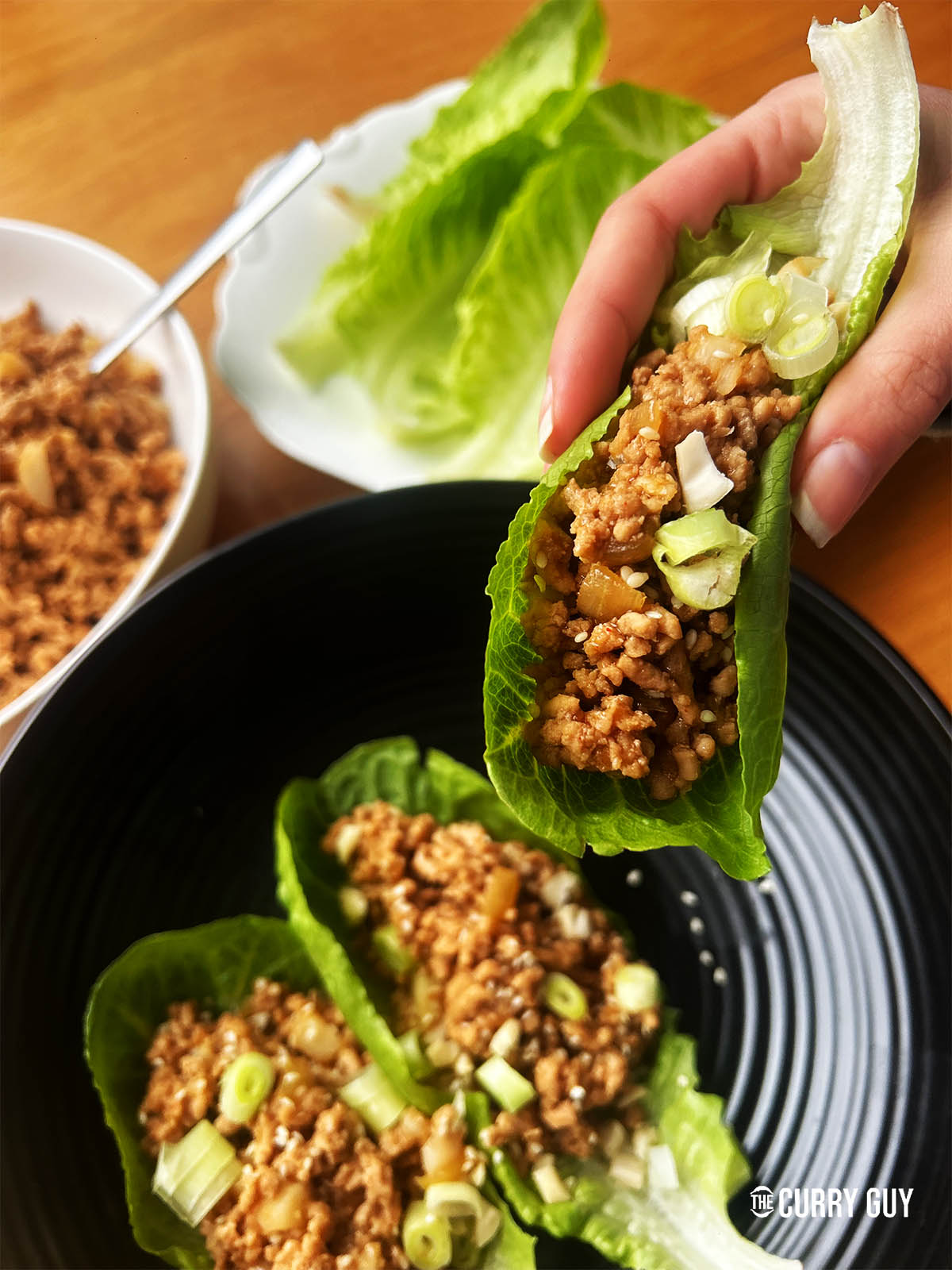 Pork lettuce wraps. Two on a plate and one being held ready to eat.