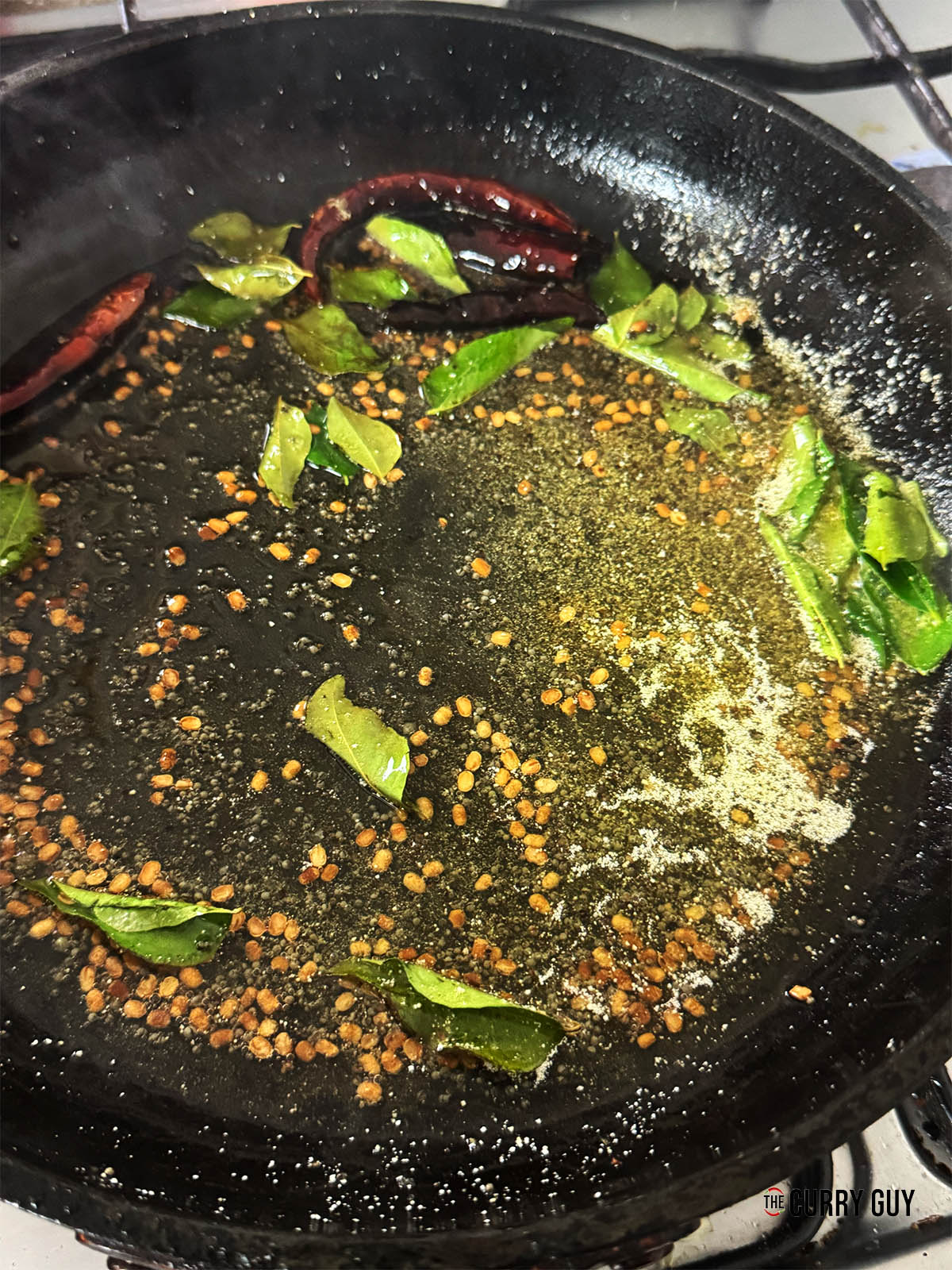 Adding the curry leaves, asafoetida and dried red chillies to the pan.