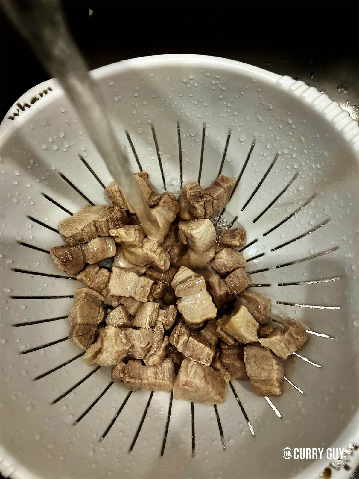 Rinsing the pork belly pieces after boiling.