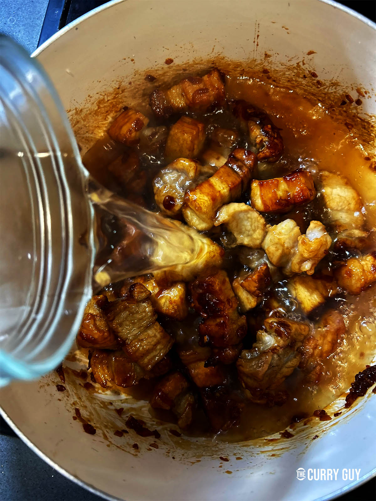 Adding the coconut water, fish sauce, soy sauce and chillies before simmering for 45 minutes.