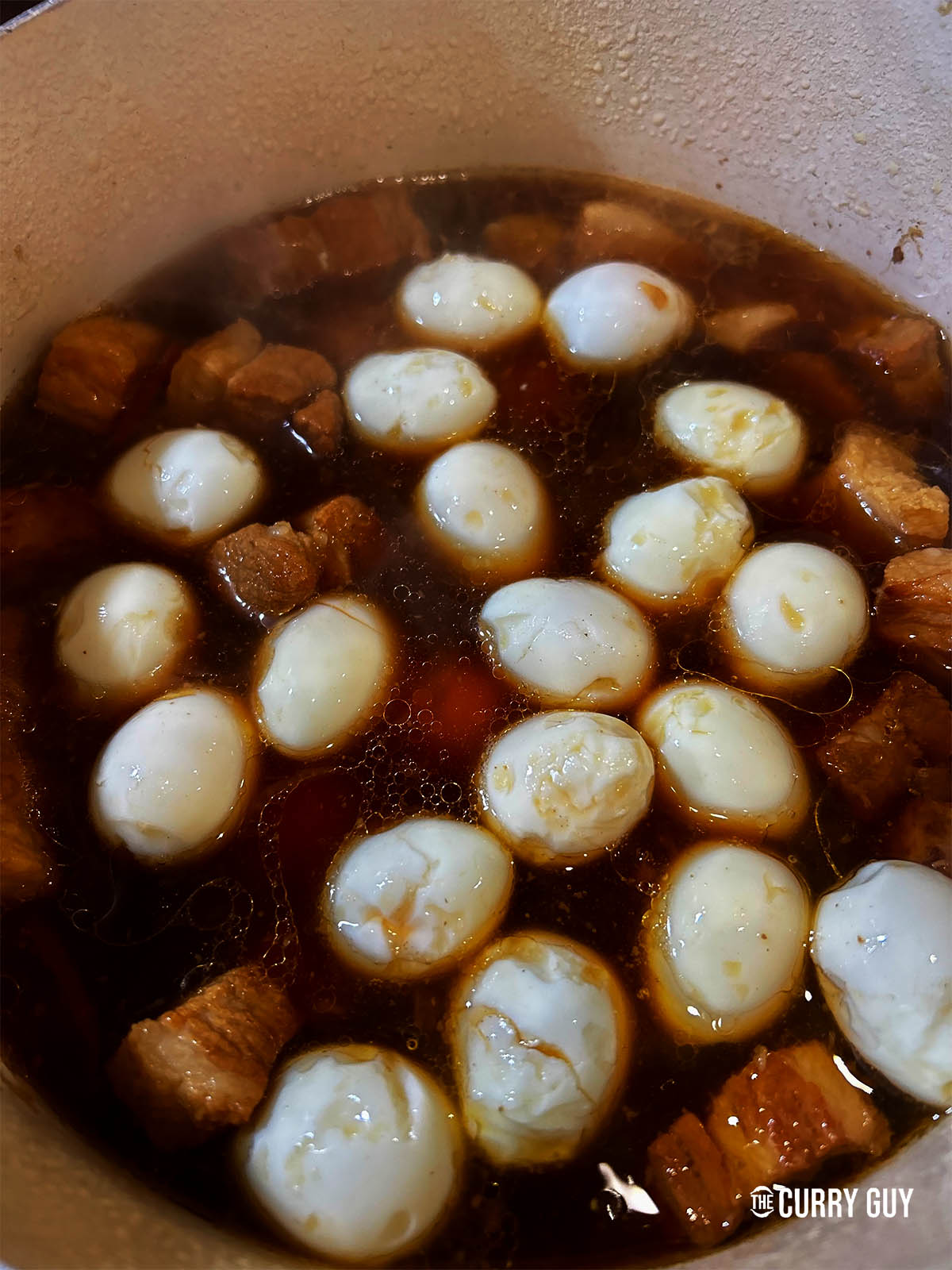 Adding the boiled eggs to the pork and sauce.