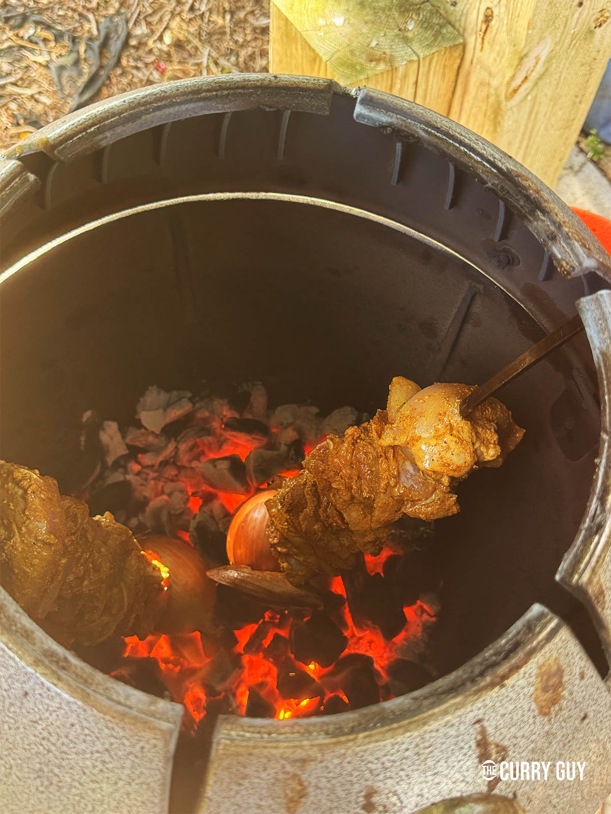 Placing two skewers of chicken shawarma into a hot tandoor oven.