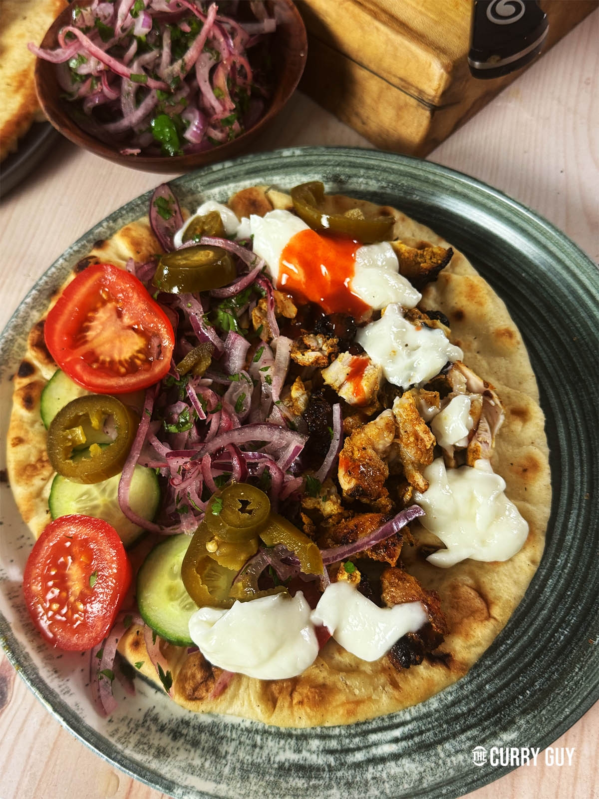 Chicken shawarma meat served on a flatbread with salad vegetables and garlic sauce.