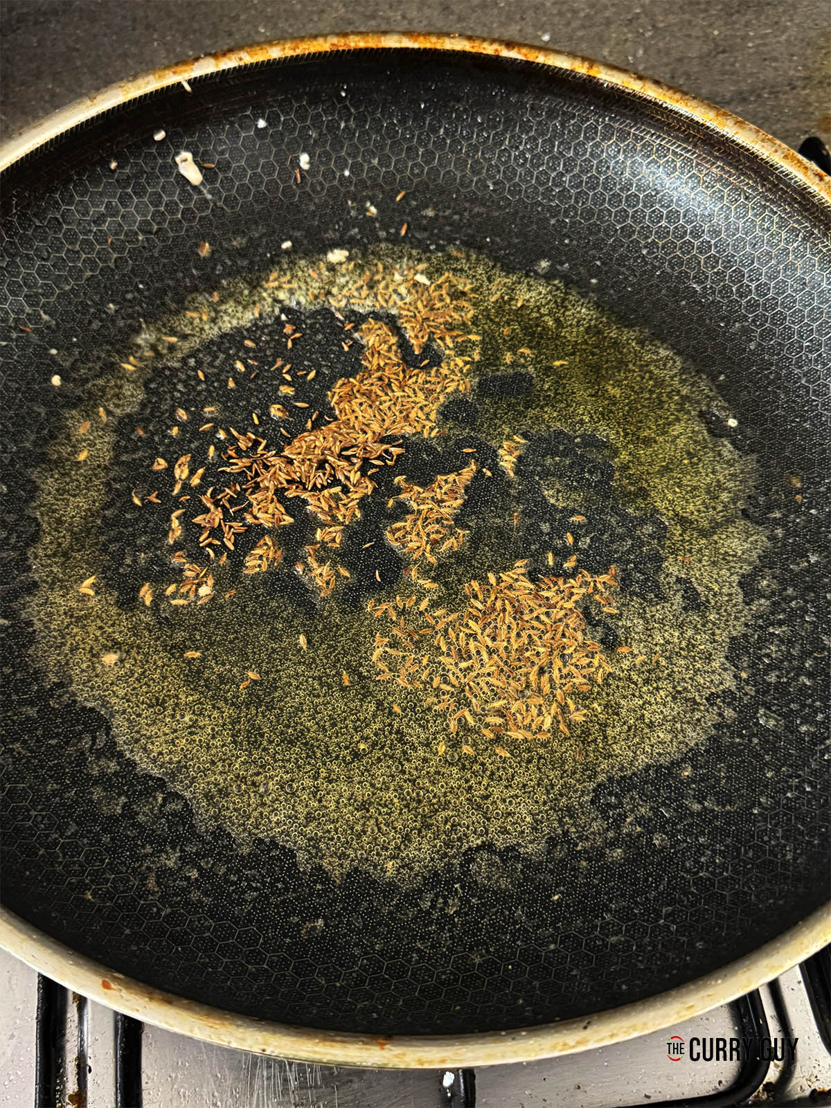 Infusing cumin seeds into hot ghee in a pan.