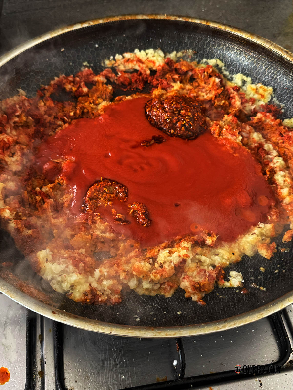 Adding the passata and naga pickle to the sauce.