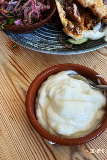 Garlic sauce in a serving bowl with a kebab in the background.