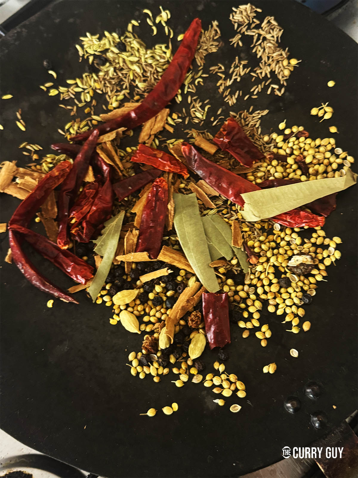 The whole spices in a frying pan toasting over a medium heat.