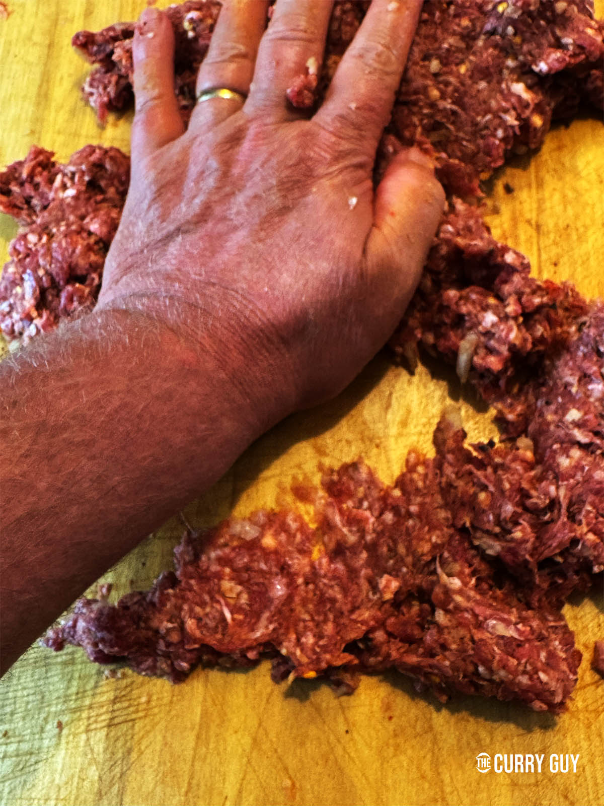 On a countertop, kneading the meat mixture