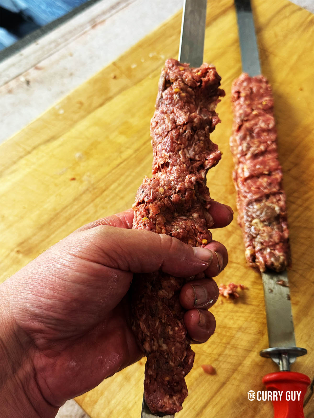 Squeezing the meat onto a flat skewer.
