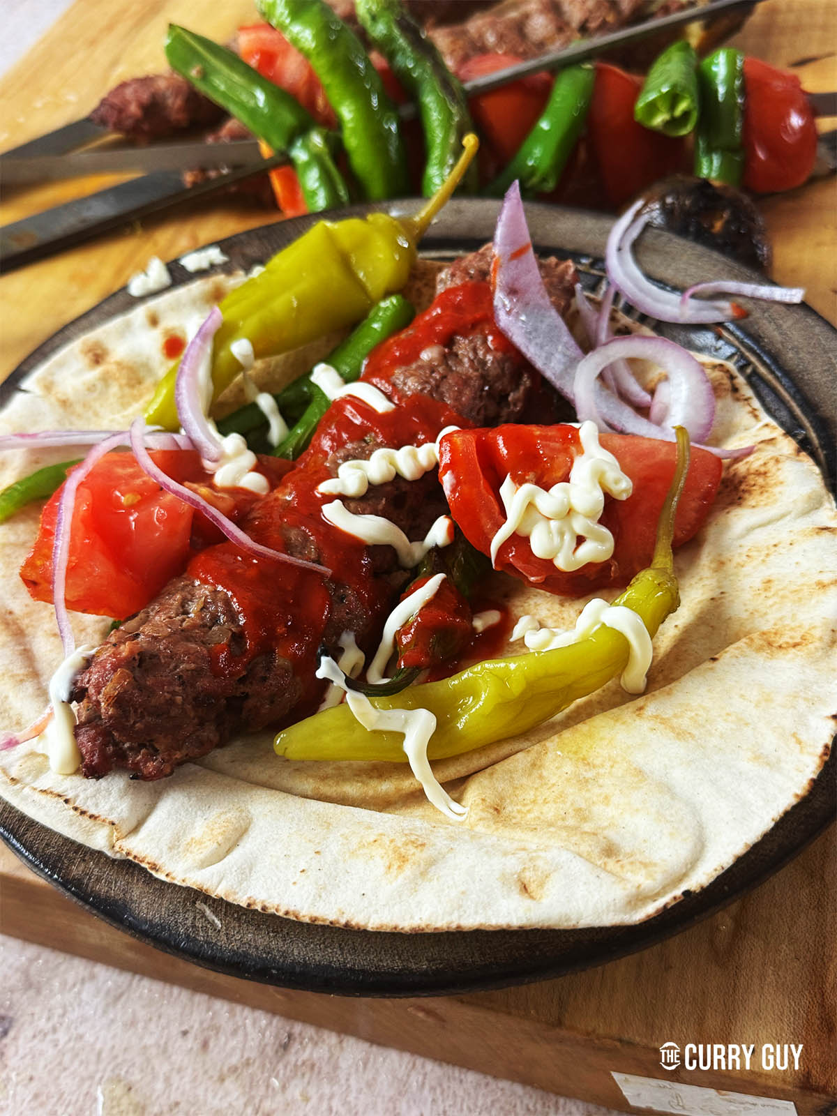 Kebab koobideh on a flatbread with sauces and salad vegetables.