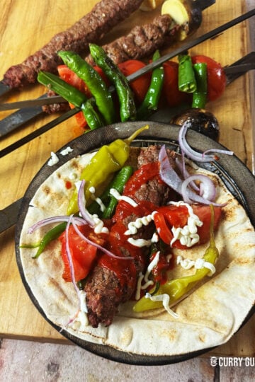 Kebab koobideh on a counter top served with flatbread, salad vegetables and kebab sauces.