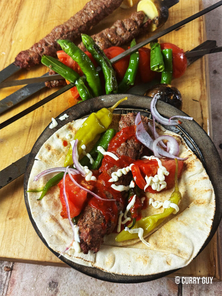 Kebab koobideh on a counter top served with flatbread, salad vegetables and kebab sauces.