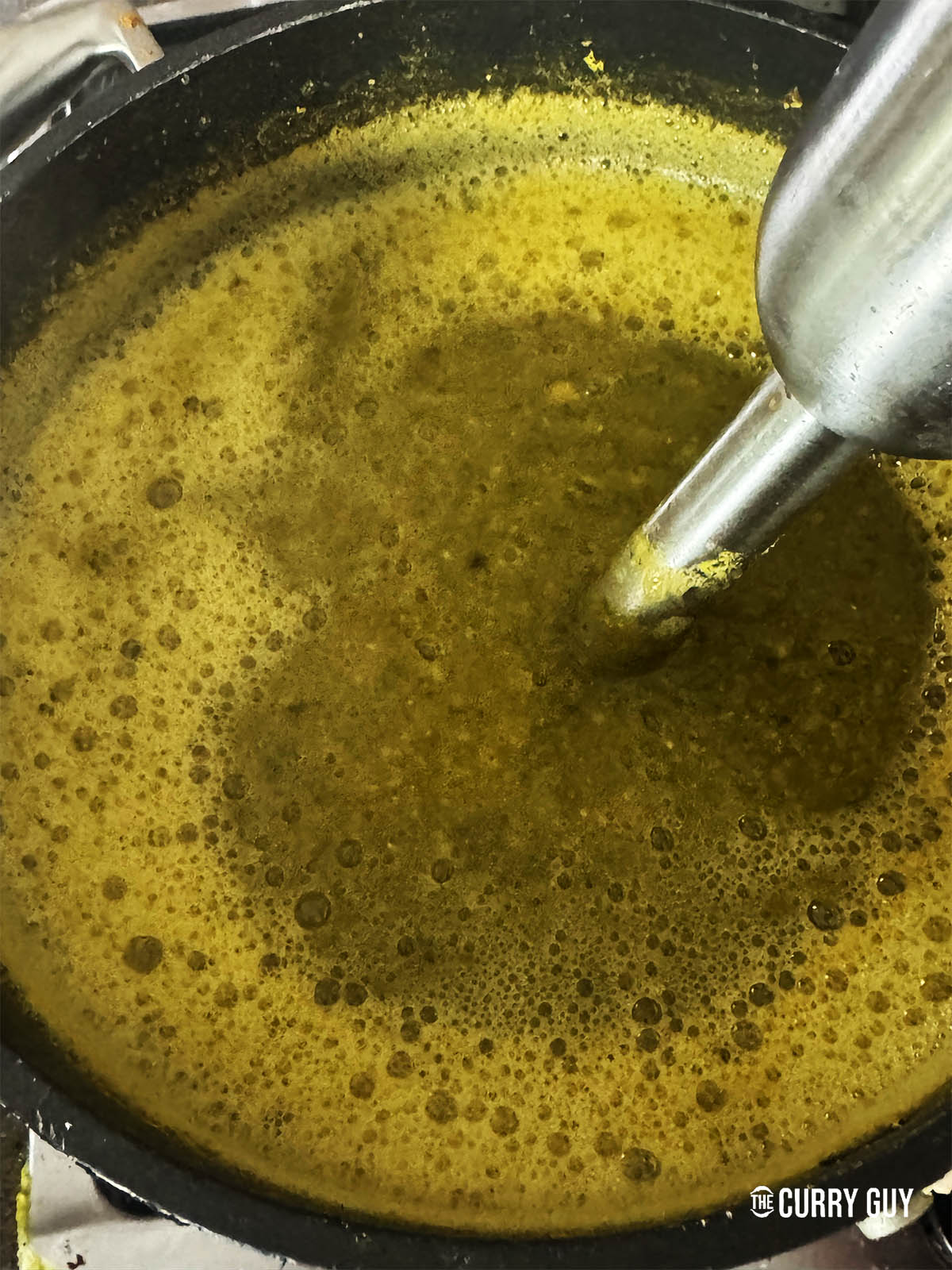 Blending the dal and vegetables in the pot with a hand-held blender.