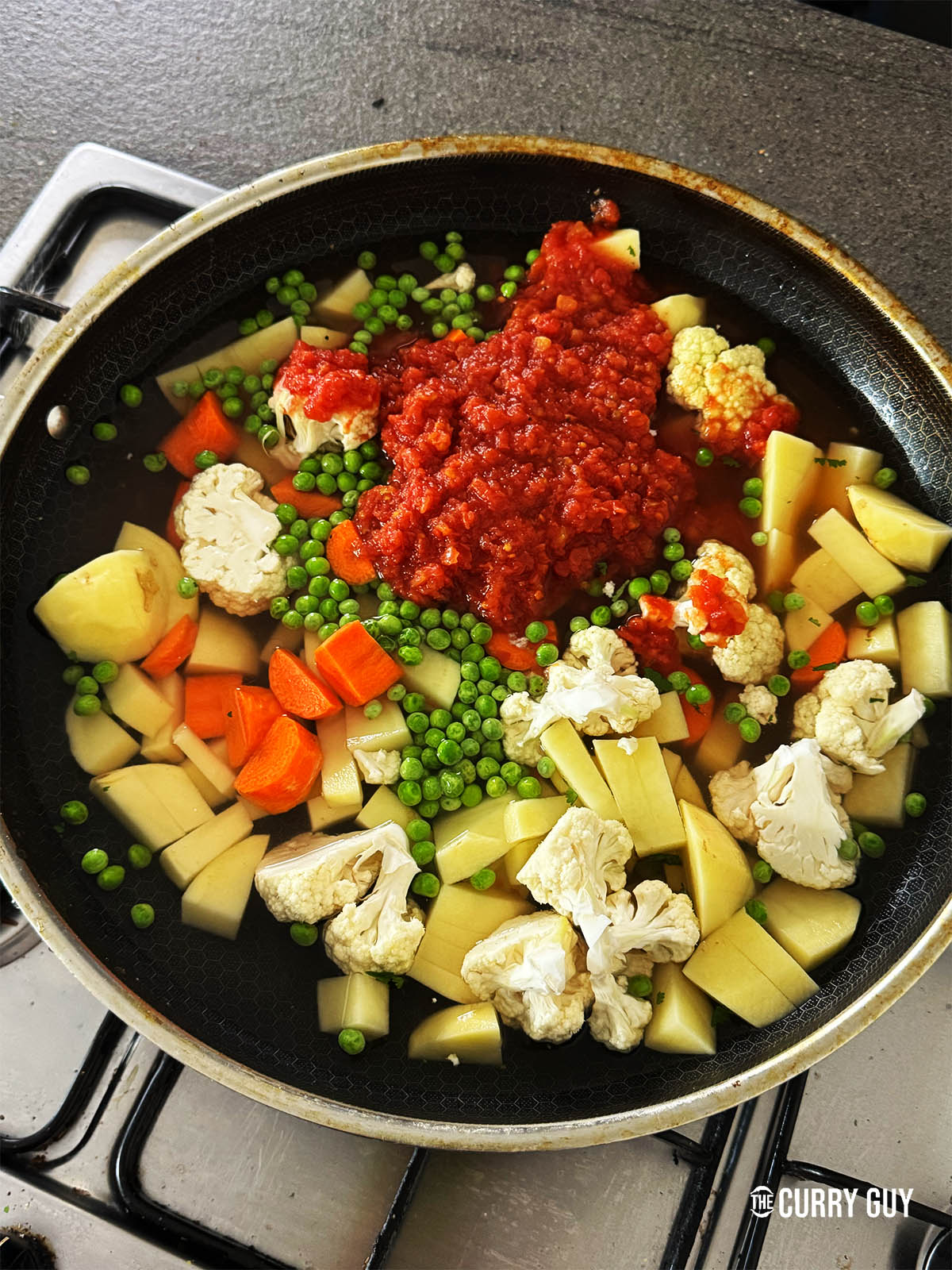 The potatoes, cauliflower, peas, carrots and chopped tomatoes in a pot.