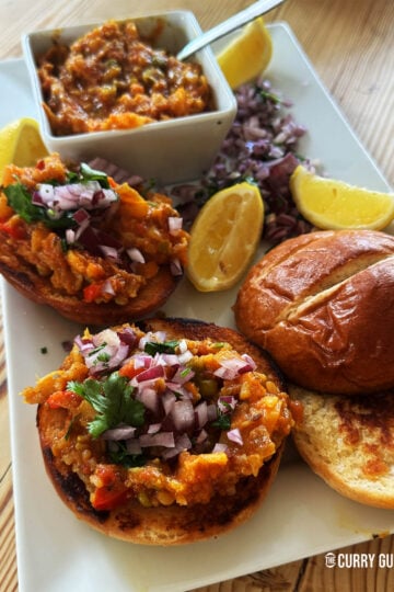 Pav Bhaji served on a plate with lemons and chopped onion garnish.