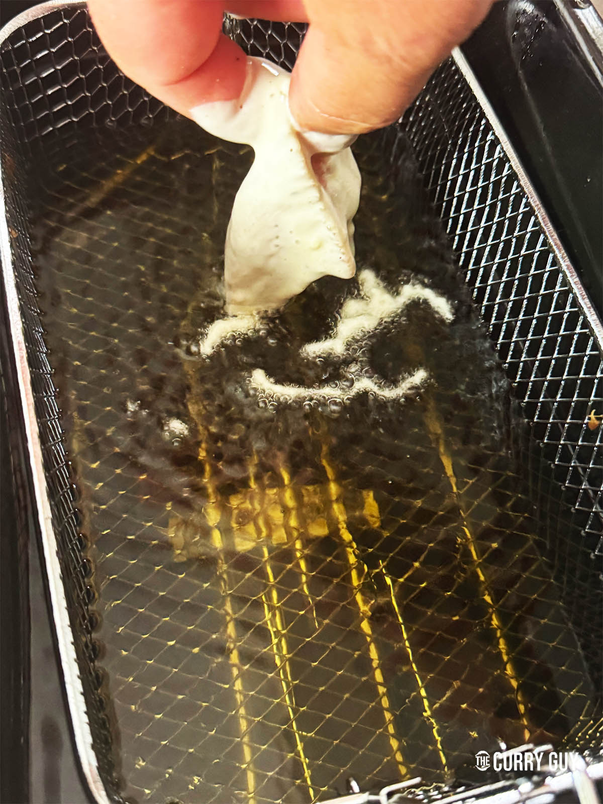 Slowly lowering a battered piece of chicken intro the oil to fry for 4 minutes