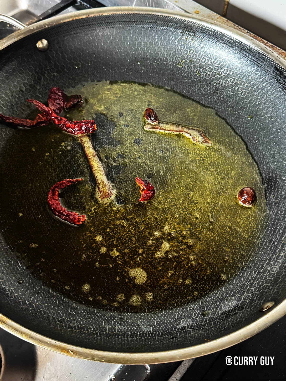 Infusing the black cardamom pods, dried Kashmiri chillies and cinnamon stick in the ghee and mustard oil in a pan over a medium-high heat. 