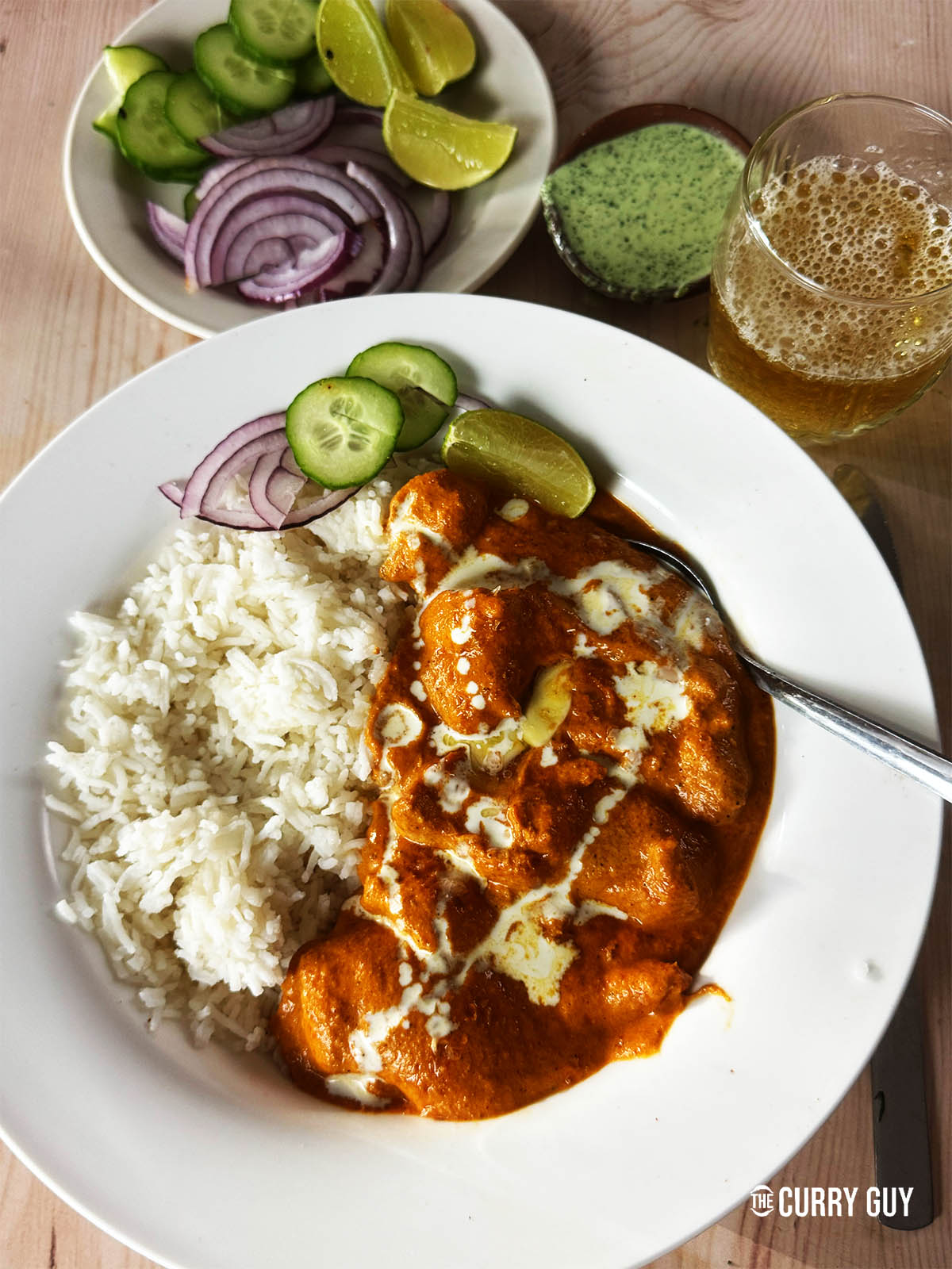 Butter chicken in a serving bowl with rice and a side of cucumber and red onion.