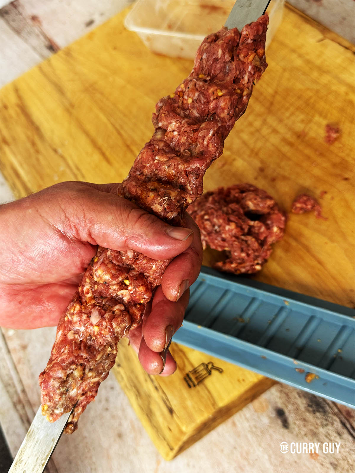 Squeezing meat onto flat skewers to cook over fire.
