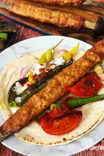 Chicken koobideh on a skewer on a plate with flatbread, salad vegetable and sauces