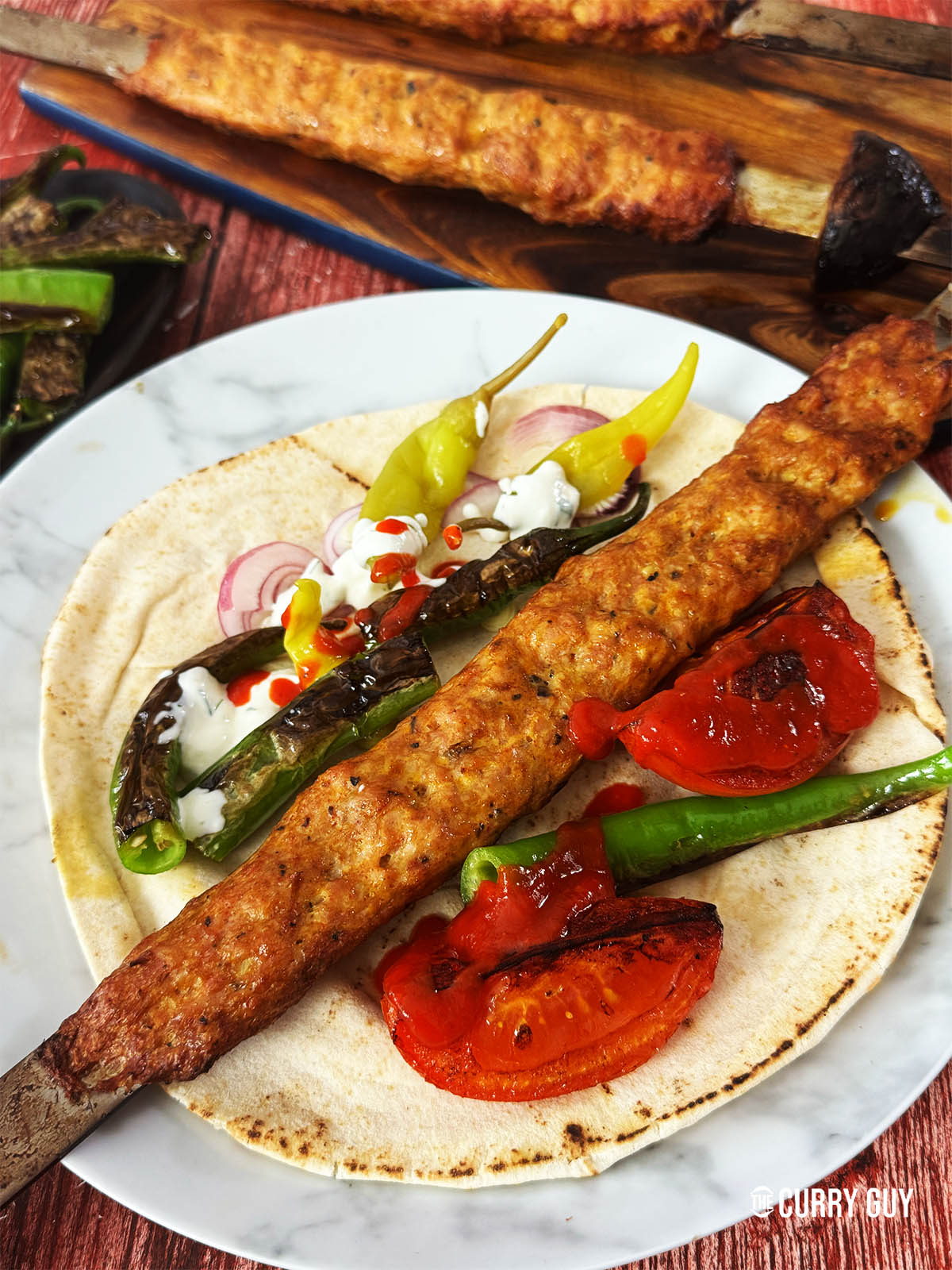 Chicken koobideh on a skewer on a plate with flatbread, salad vegetable and sauces