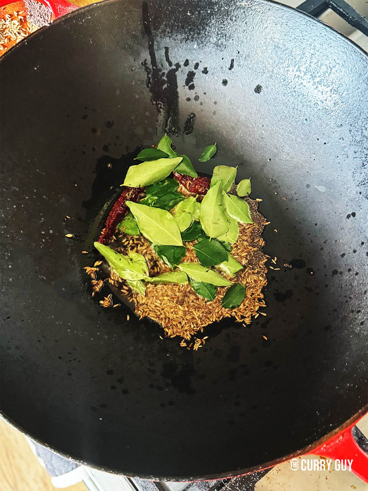 Adding the dried chillies, cumin seeds and curry leaves to the pan to infuse their flavour into the oil. 