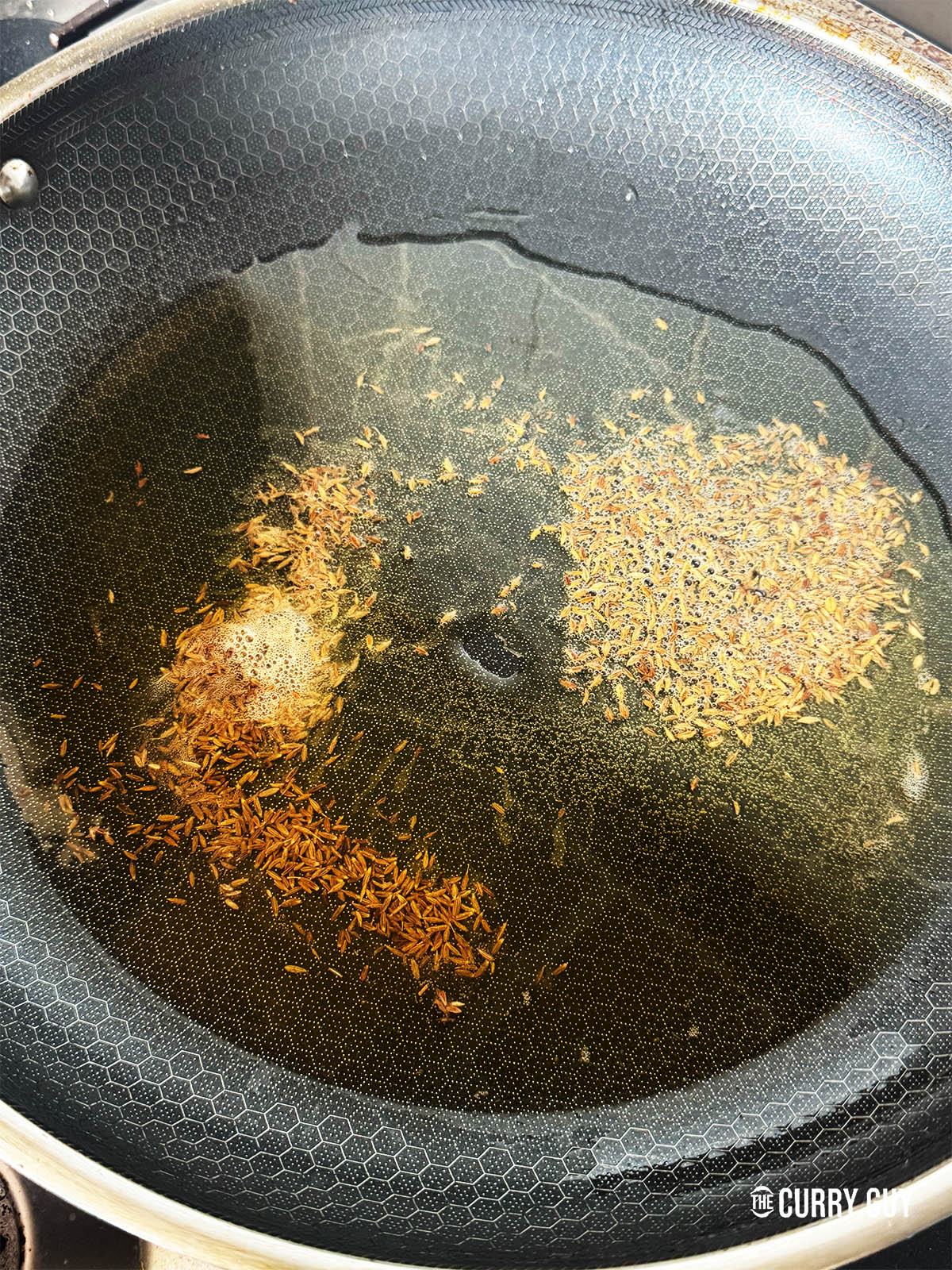 Infusing cumin seeds into hot oil and ghee in a pan.