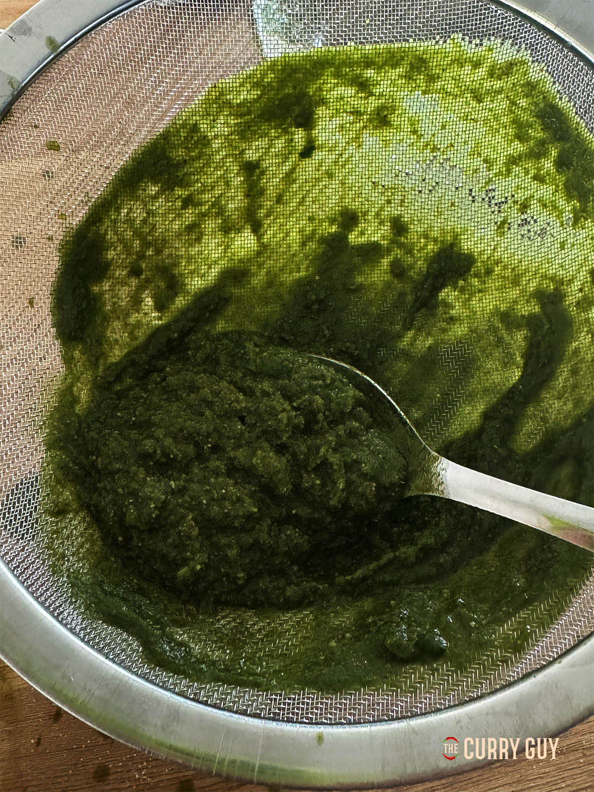 Scrape the herb mixture through the sieve by pressing down and scraping with a spoon.