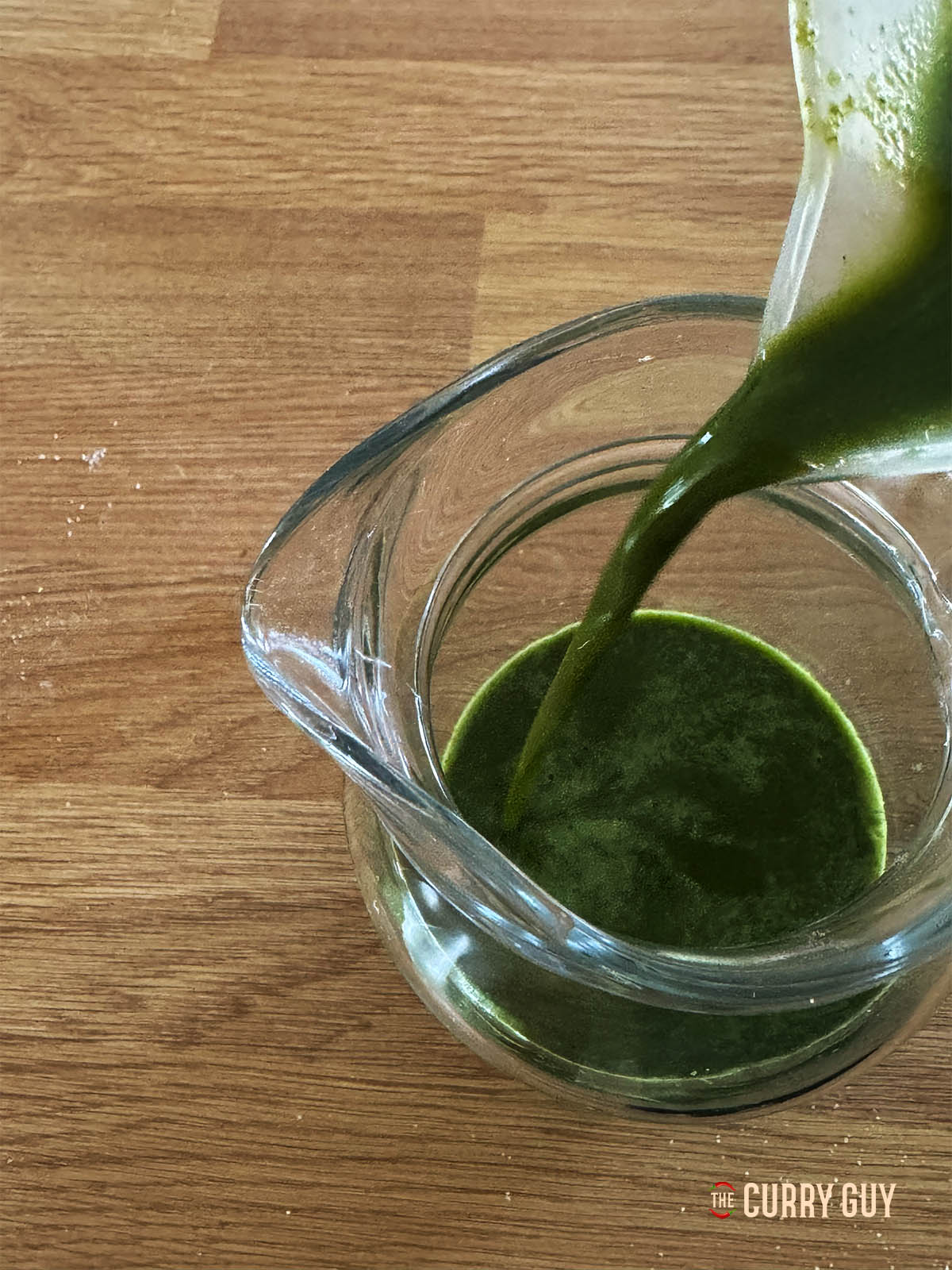 Pouring the green pani front a plastic spout to a glass serving jar.