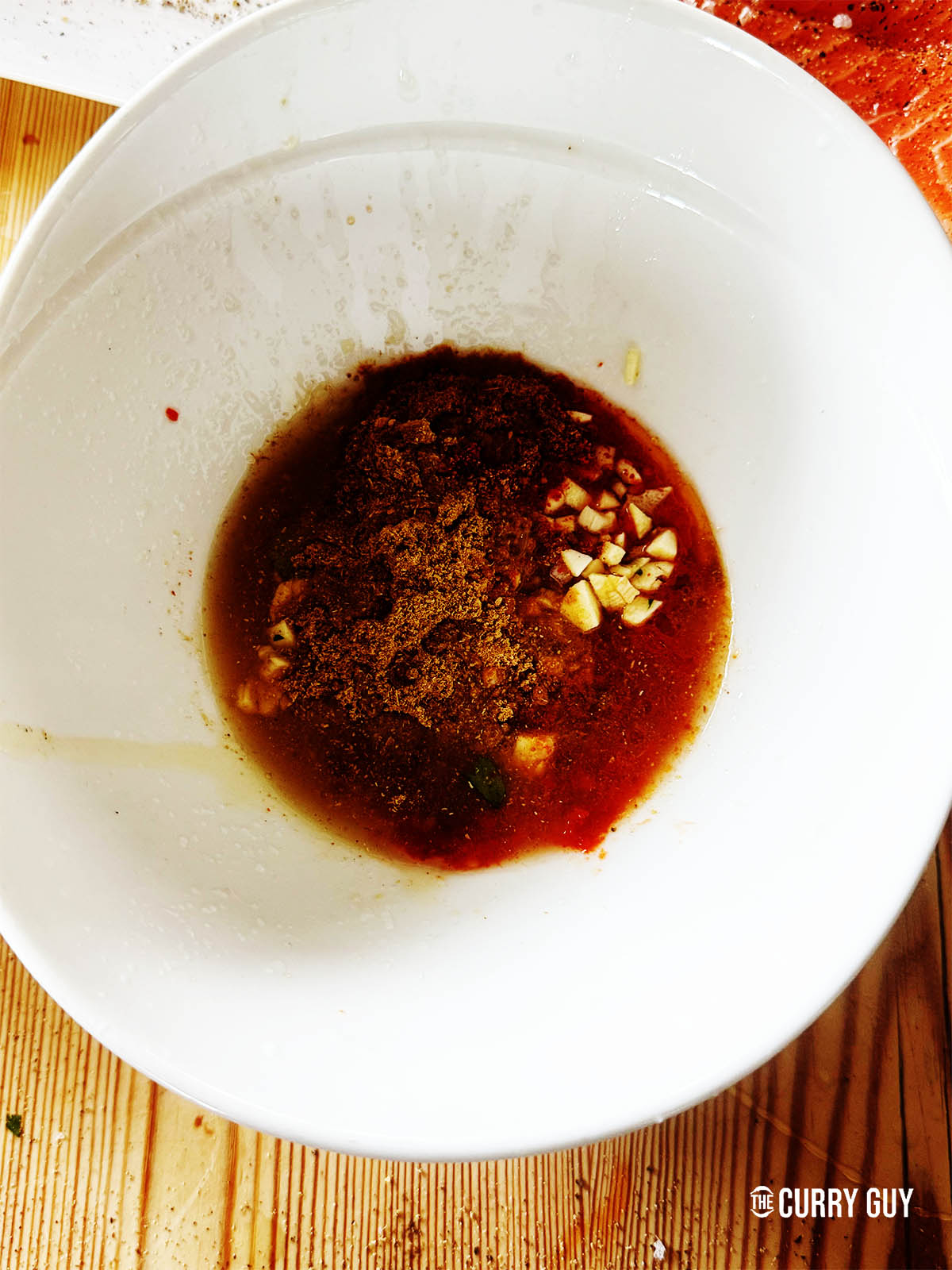 The harissa paste in a bowl with the garlic, olive oil, honey, lime juice, Aleppo pepper, coriander, cumin and ground ginger. 