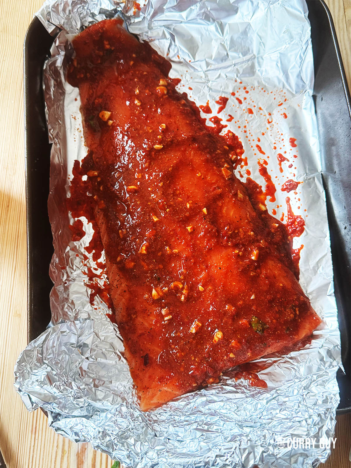 Spreading the harissa paste under and over the salmon on the foil