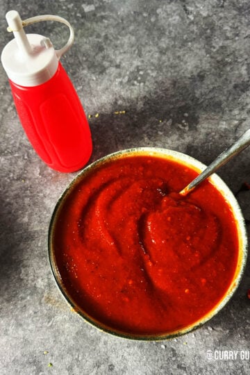 Red kebab shop sauce in a serving bowl next to a squeeze bottle.