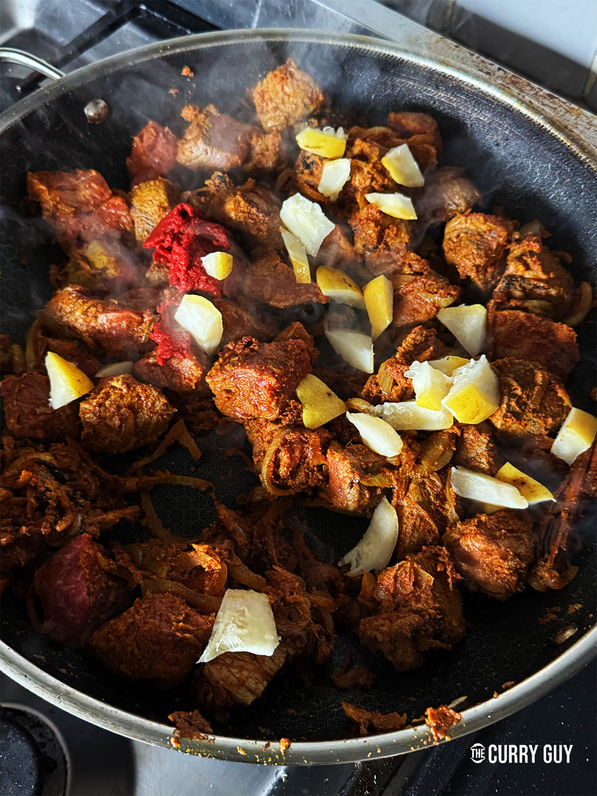 Adding the shatkora and tomato puree to the pan before stirring them in. 