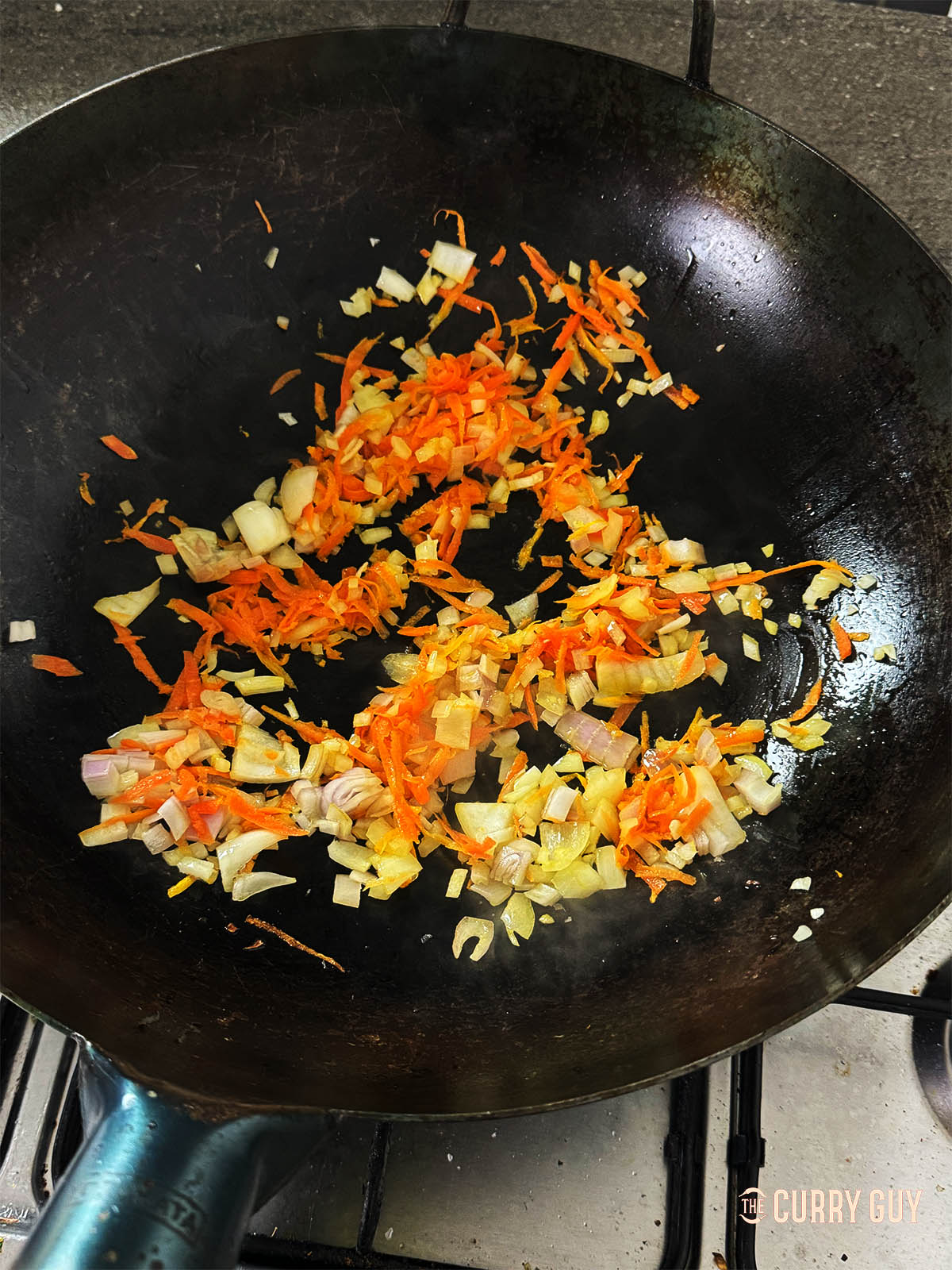 Frying the onions and grated carrot in a wok.