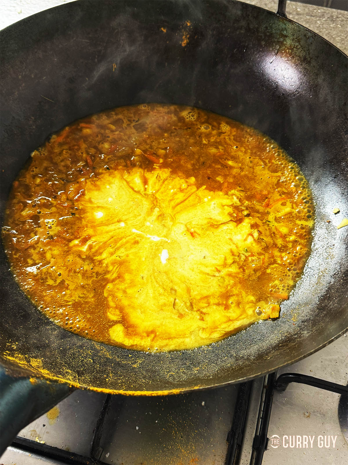 Adding the stock and coconut milk to the wok to make a sauce.