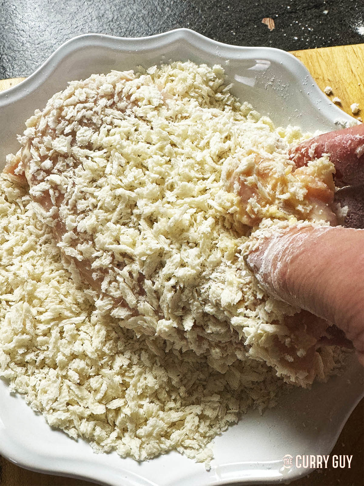 Rolling a chicken breast in panko bread crumbs.