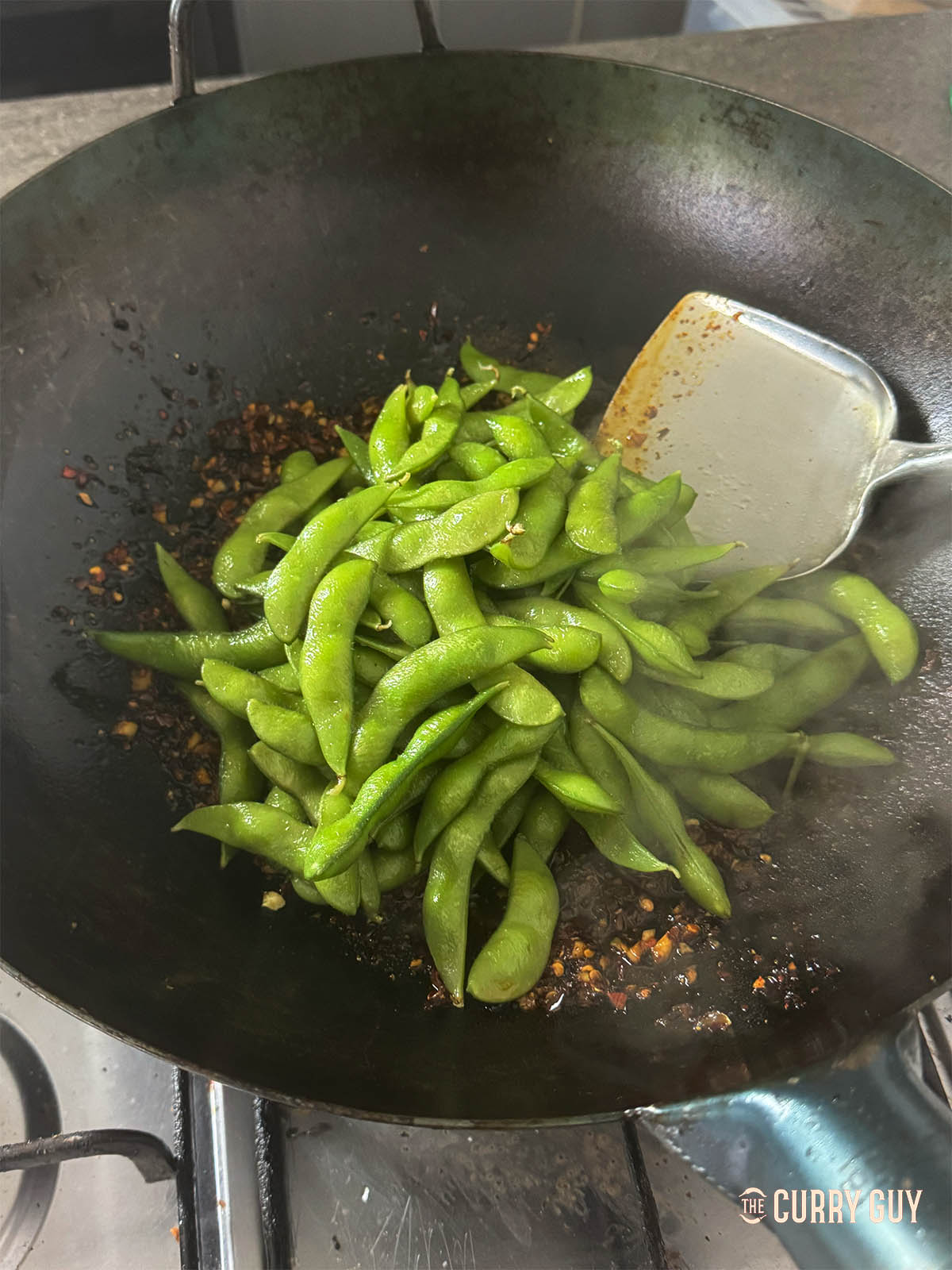 Adding the cooked edamame to the wok.